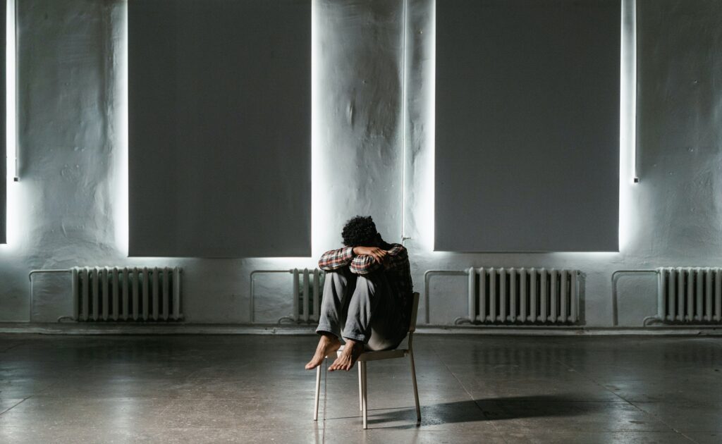 Man sitting on a chair with his head buried in his arms.